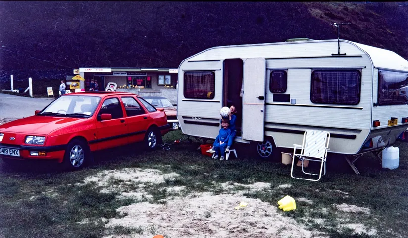 Restored slide of a car and caravan at a campsite, with a child in the caravan doorway